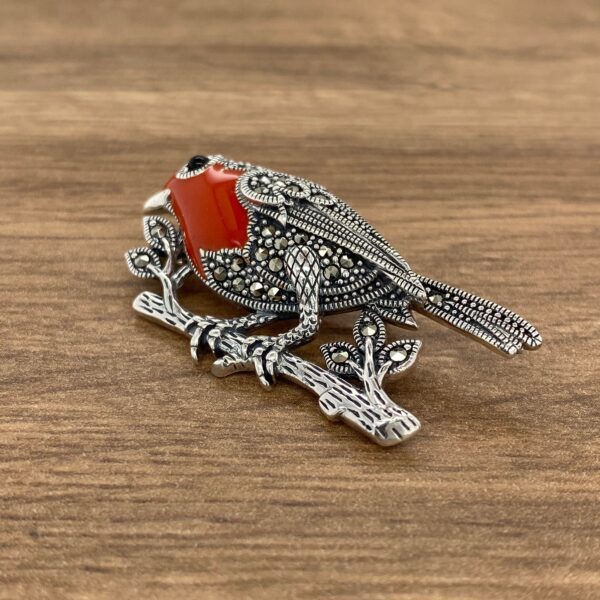 Silver robin brooch with red gemstone.