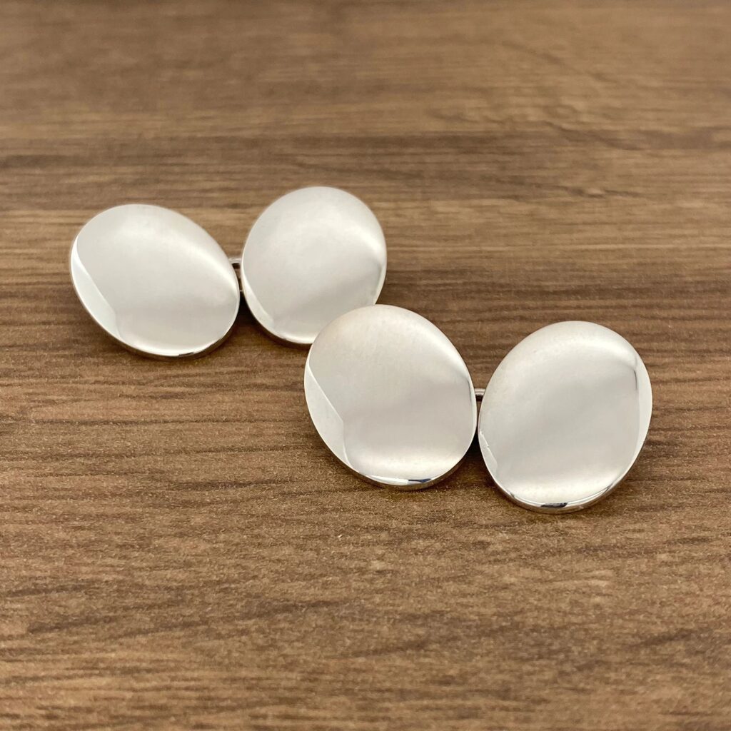 Two silver cufflinks on a wooden table.