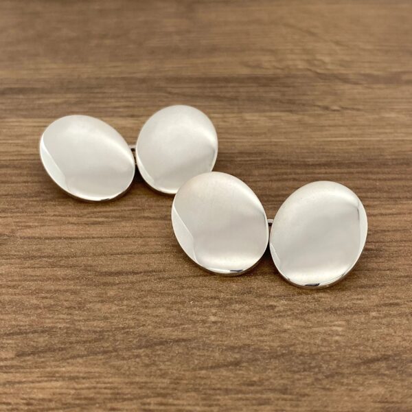 Two silver cufflinks on a wooden table.