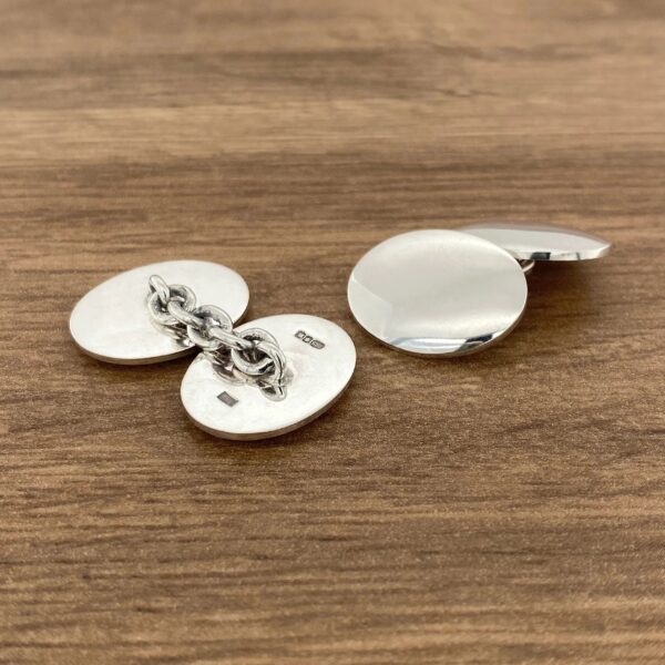 Silver round cufflinks on wooden surface.