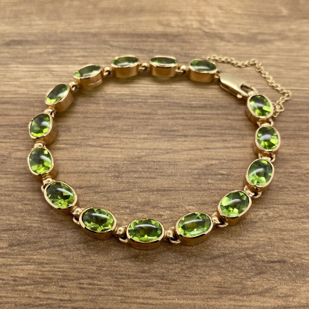 An oval peridot bracelet on a wooden table.