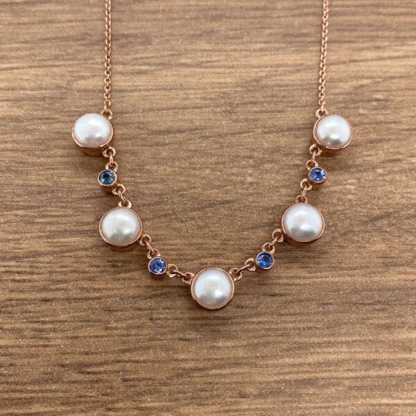 Pearl and sapphire necklace on wooden background.