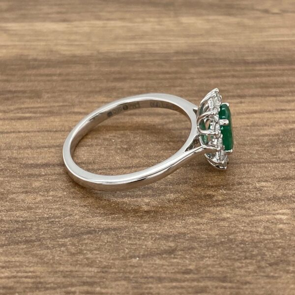 Emerald and diamond halo ring on wood background.