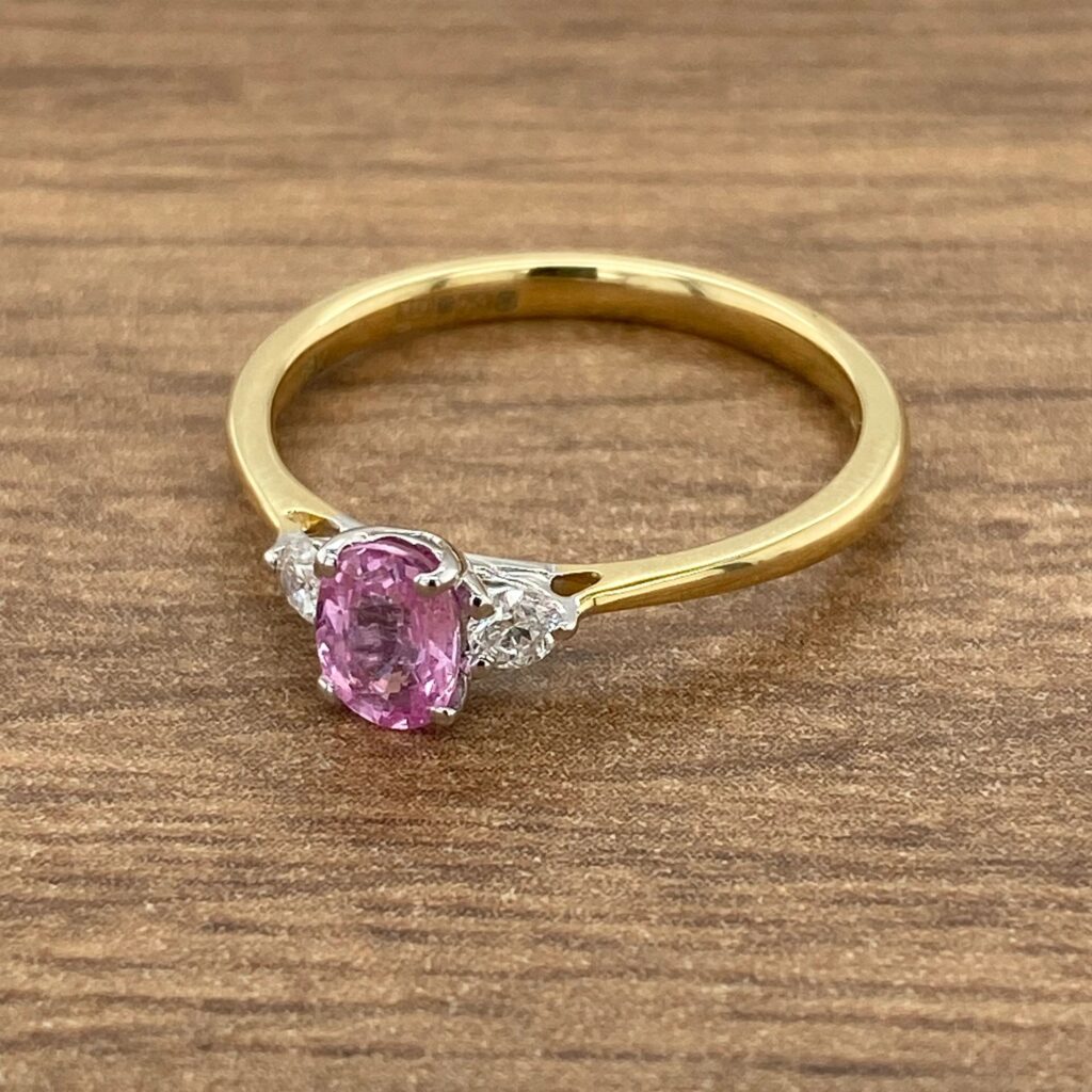 Pink sapphire and diamond ring on wood.