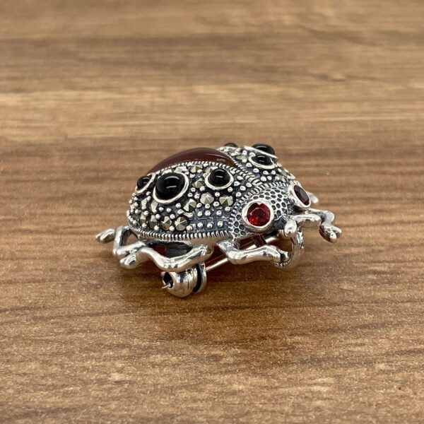 Silver ladybug brooch with black and red stones.