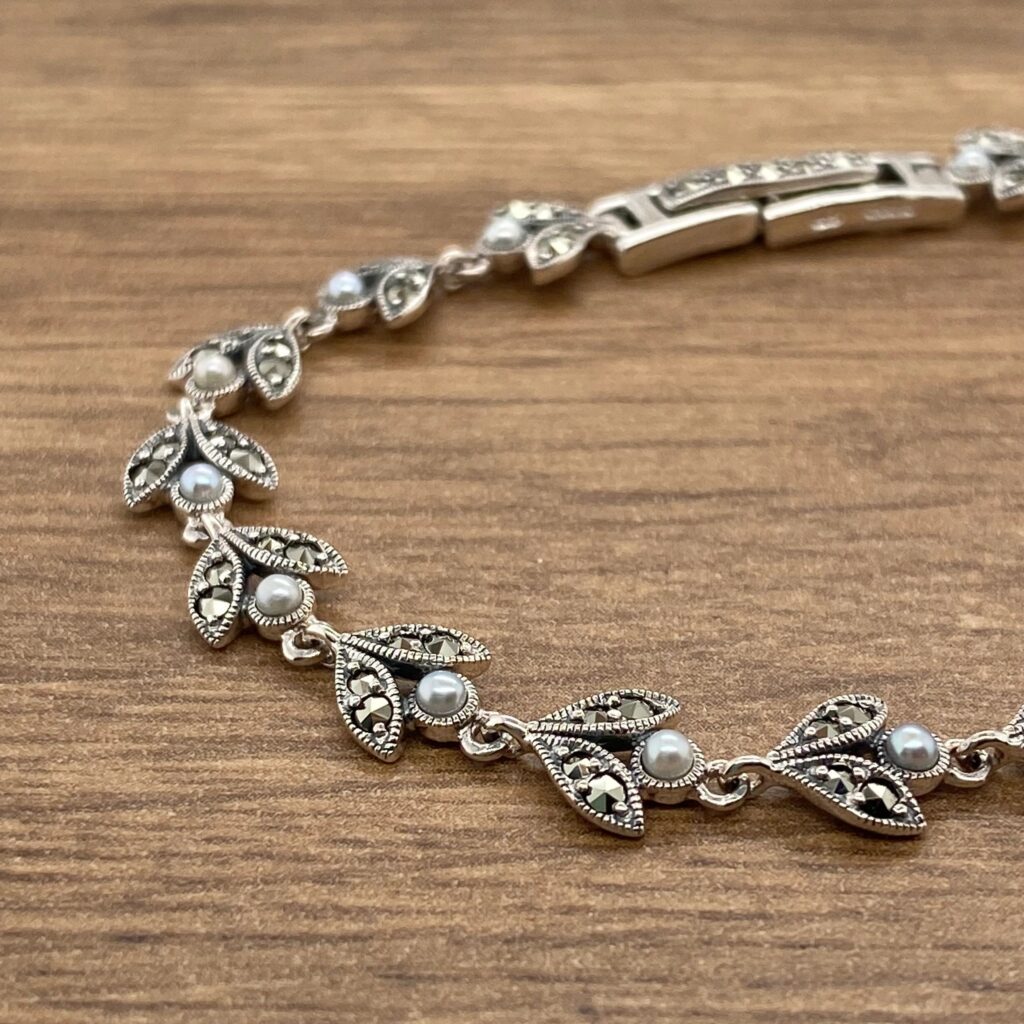 A silver bracelet with leaves and pearls on a wooden table.