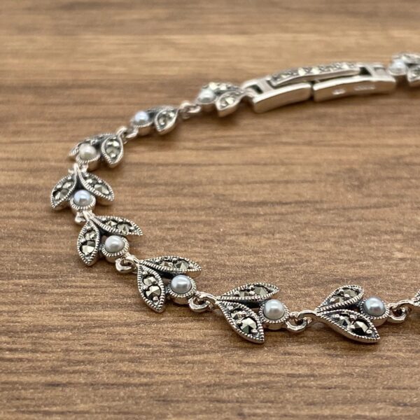 A silver bracelet with leaves and pearls on a wooden table.