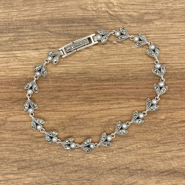 A silver bracelet with leaves and pearls on a wooden table.