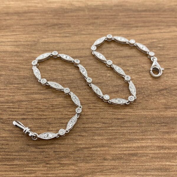 A silver bracelet with diamonds on it with a wooden background.