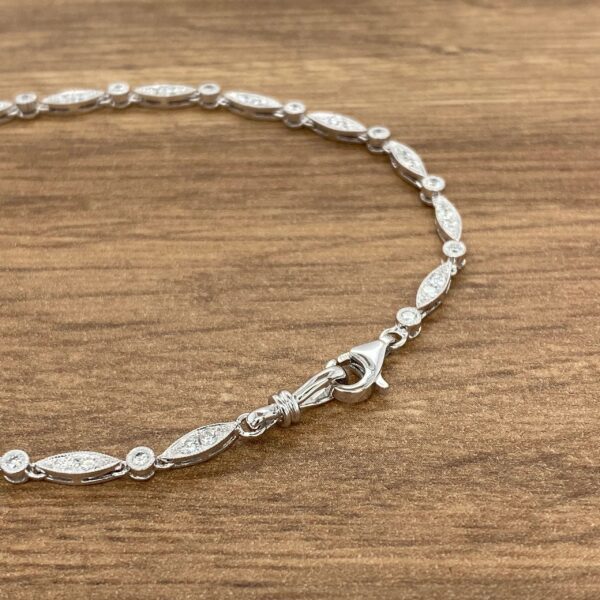 A silver bracelet with diamonds on it with a wooden background.