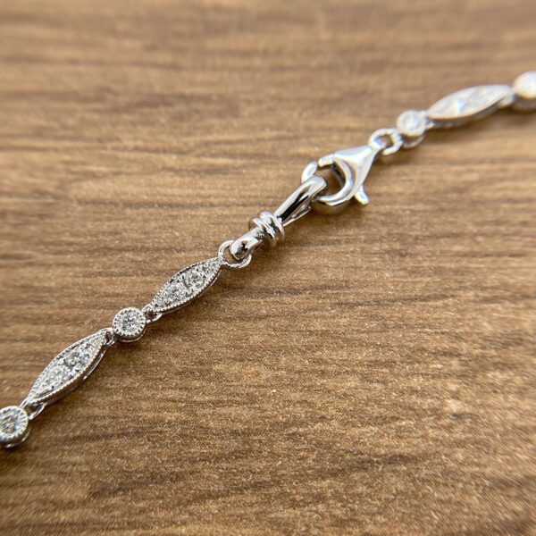 A silver bracelet with diamonds on it with a wooden background.