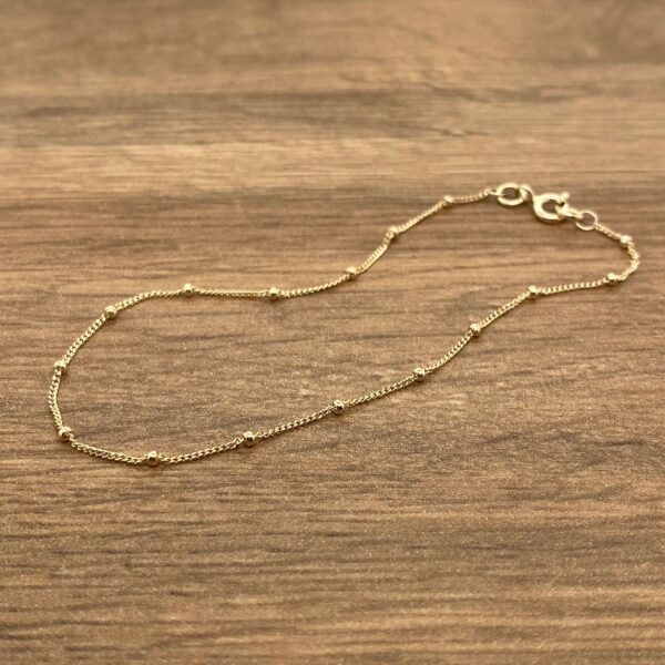 A gold beaded bracelet on a wooden table.