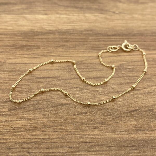 A gold beaded bracelet on a wooden table.