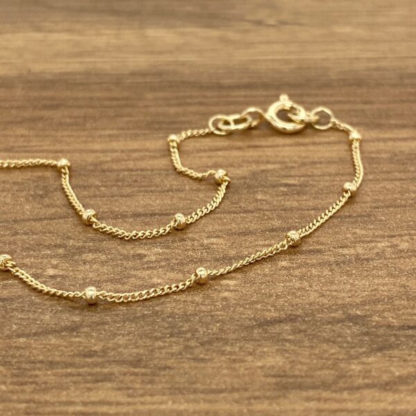 A gold beaded bracelet on a wooden table.