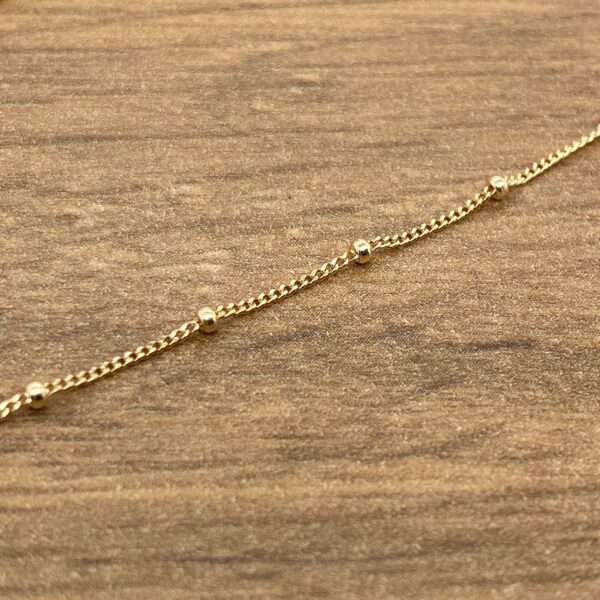A gold beaded bracelet on a wooden table.