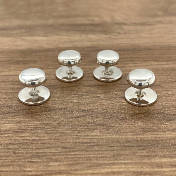 Four silver shirt studs on wood.