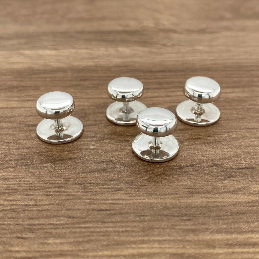 Four silver shirt studs on wood.