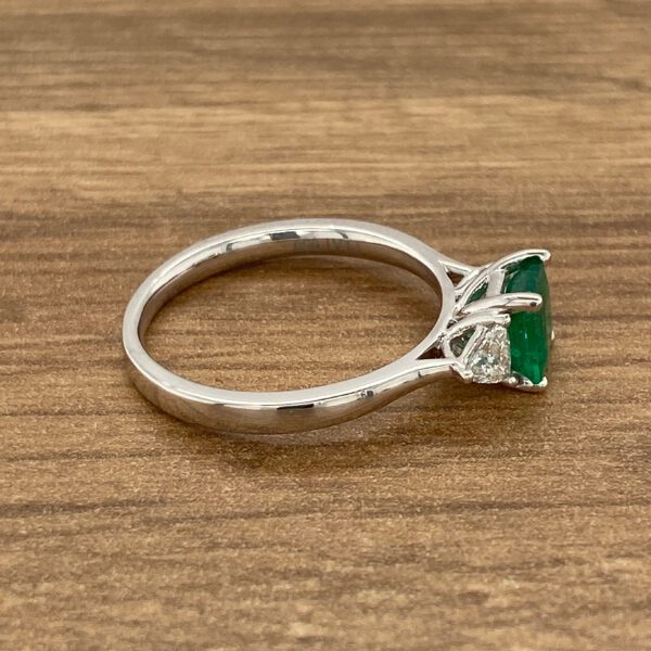 Emerald and diamond engagement ring on wood.