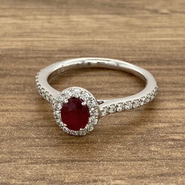 An oval ruby and diamond ring on a wooden table.