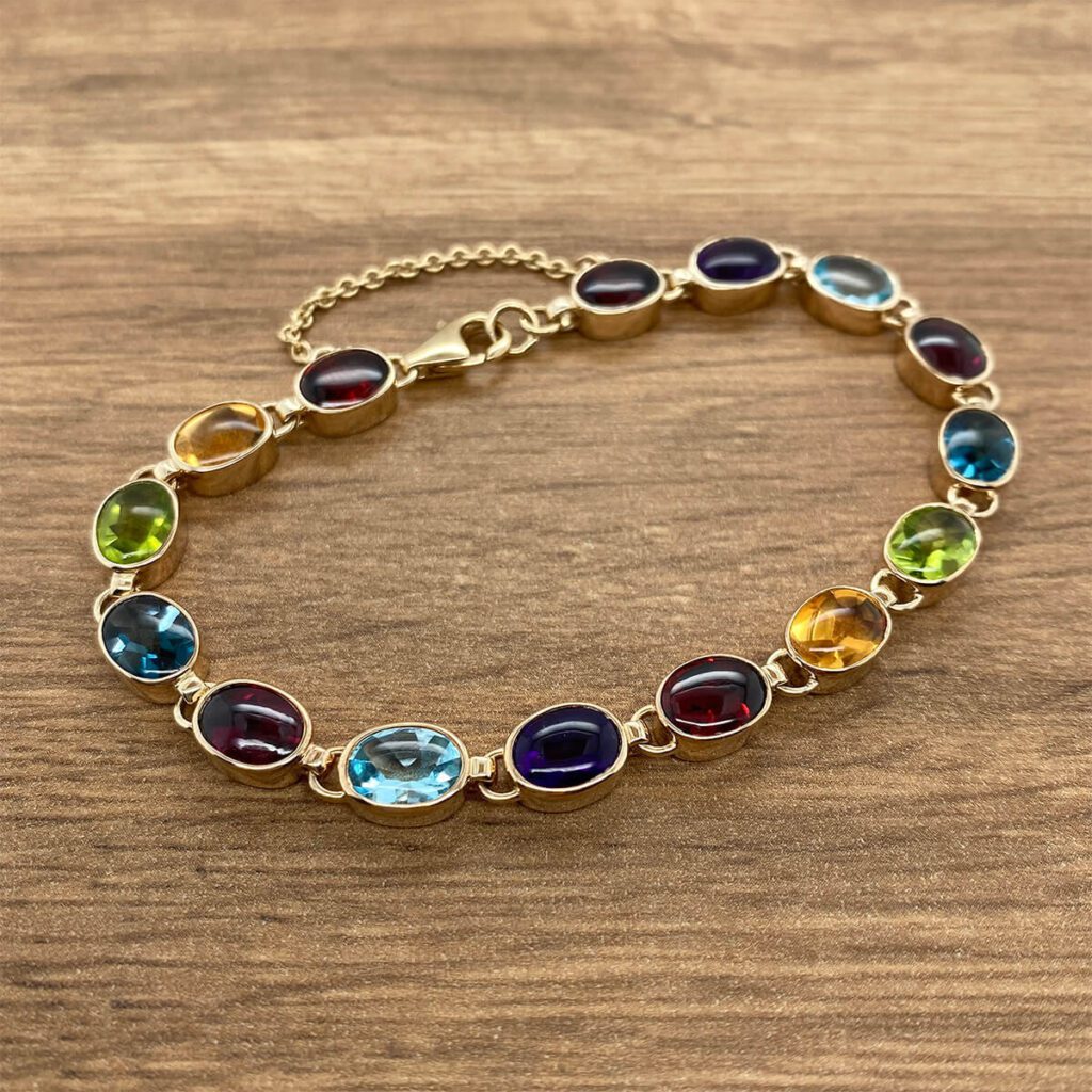 A Multigem Collet Set Bracelet with multi colored stones on a wooden table.