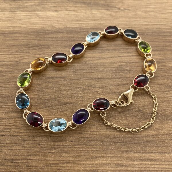 A Multigem Collet Set Bracelet with multi colored stones on a wooden table.