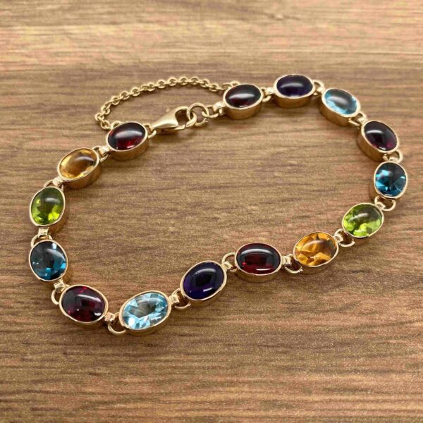 A Multigem Collet Set Bracelet with multi colored stones on a wooden table.