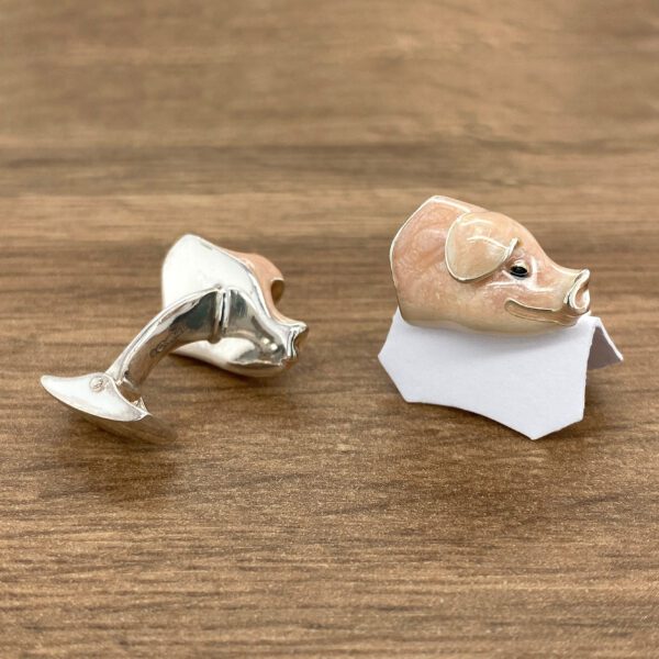 Silver pig cufflinks on a wooden surface.