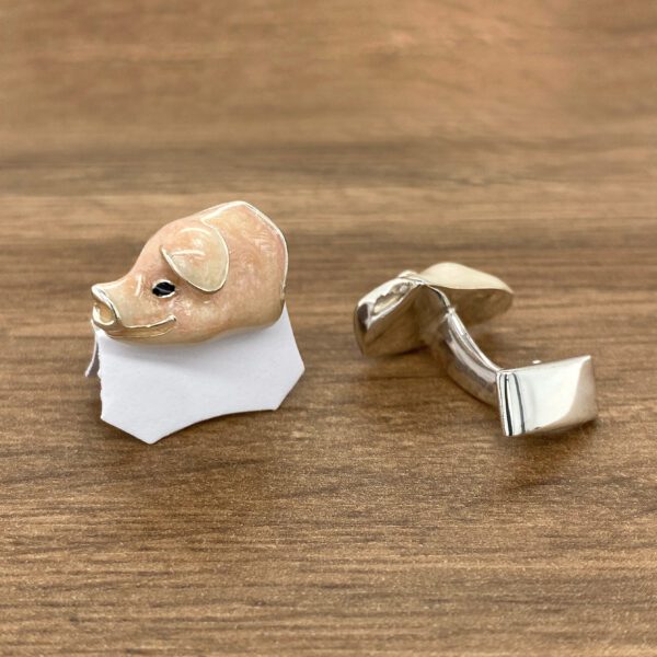 Silver pig cufflinks on wood table.