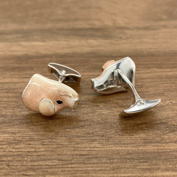 Pink pig-shaped cufflinks on wood.