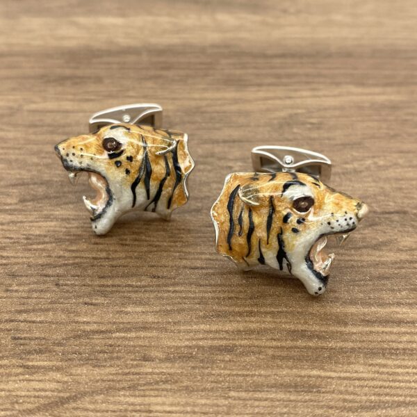 Tiger head cufflinks on wooden surface.