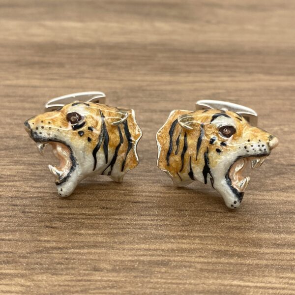 Tiger head cufflinks on wood background.