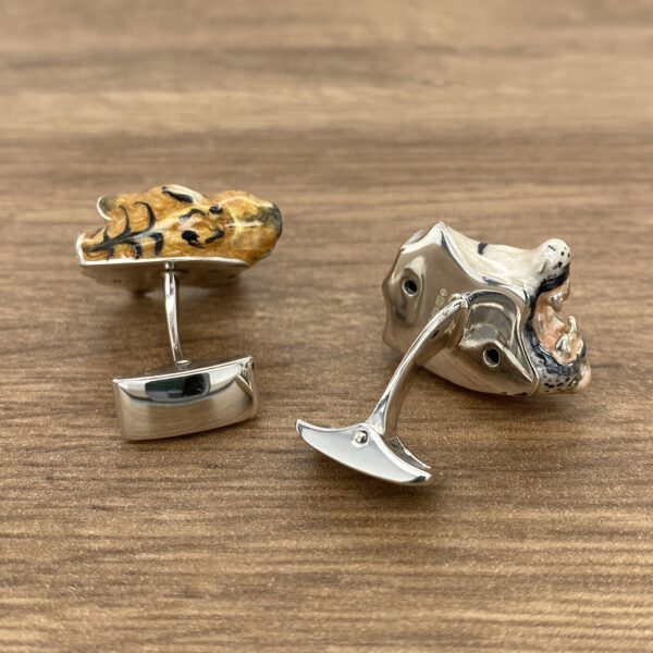 Silver tiger head cufflinks on wood.