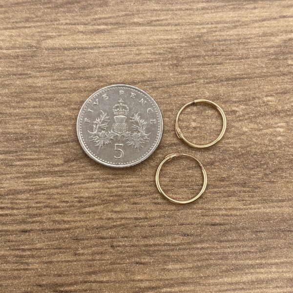 Two gold hoop earrings next to a five pence coin.