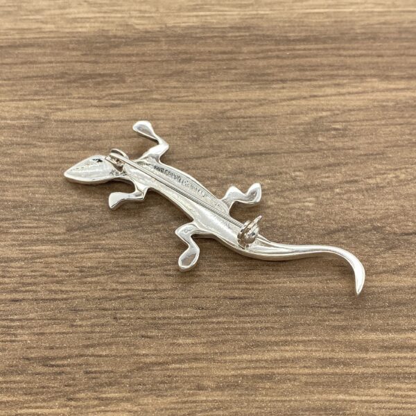 Silver lizard brooch on a wooden surface.