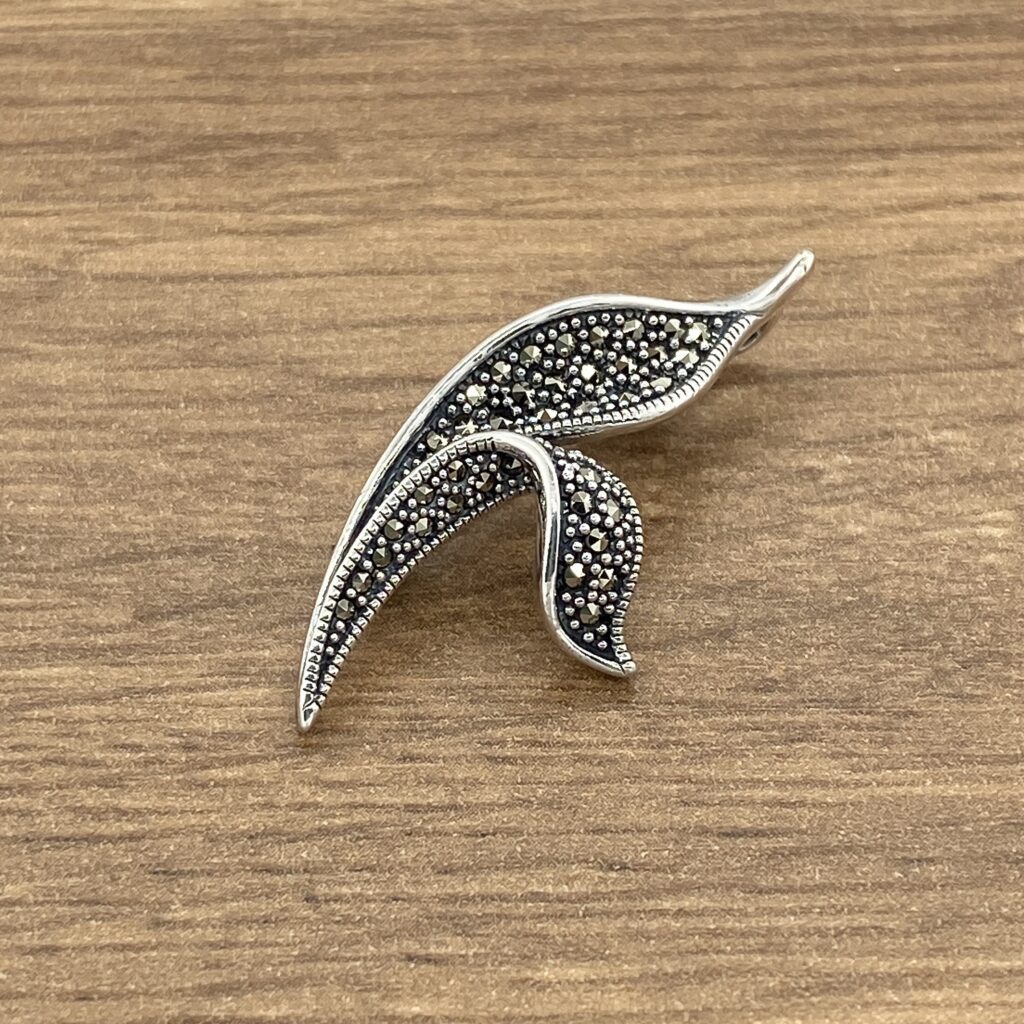 A silver leaf brooch on a wooden table.