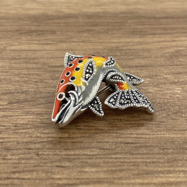 A colorful fish brooch on a wooden table.