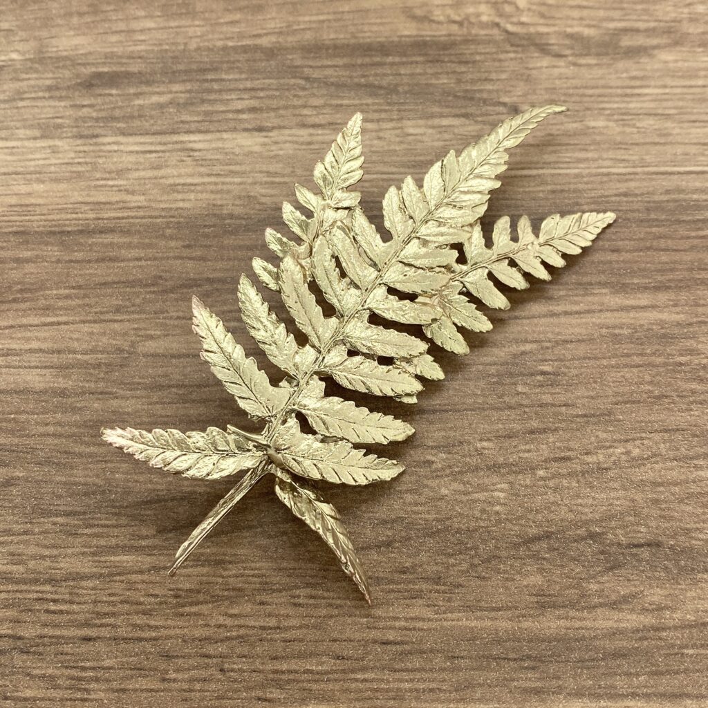 A gold fern leaf brooch on a wooden table.
