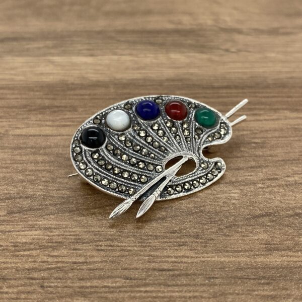 Silver artist palette brooch with gems.