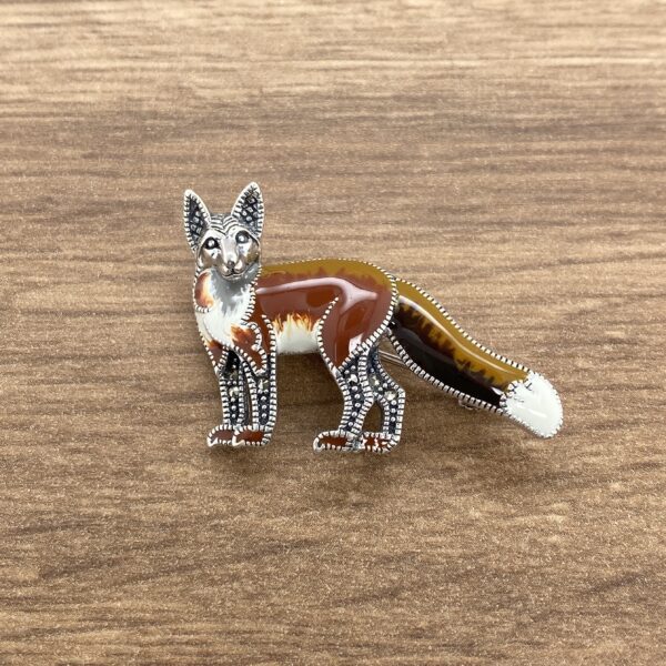 A Silver & Marcasite Enamel Fox Brooch on a wooden table.