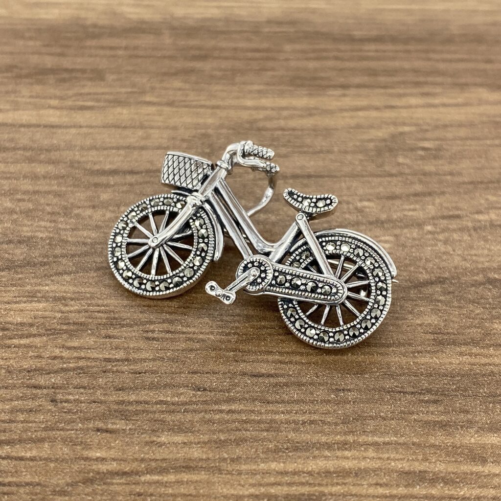A silver bicycle brooch on a wooden table.