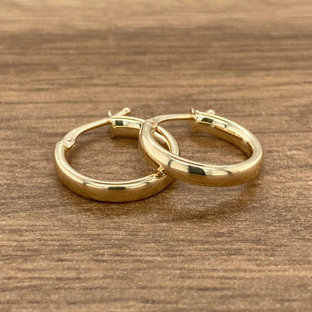 Gold hoop earrings on wooden surface.