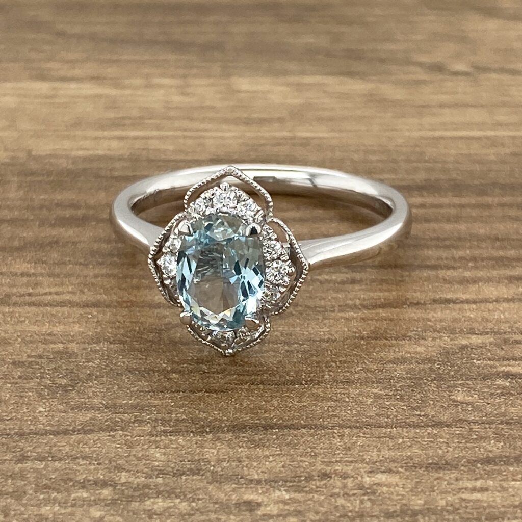 An oval aquamarine and diamond ring on a wooden table.