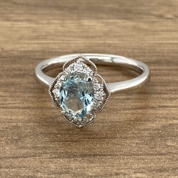 An oval aquamarine and diamond ring on a wooden table.