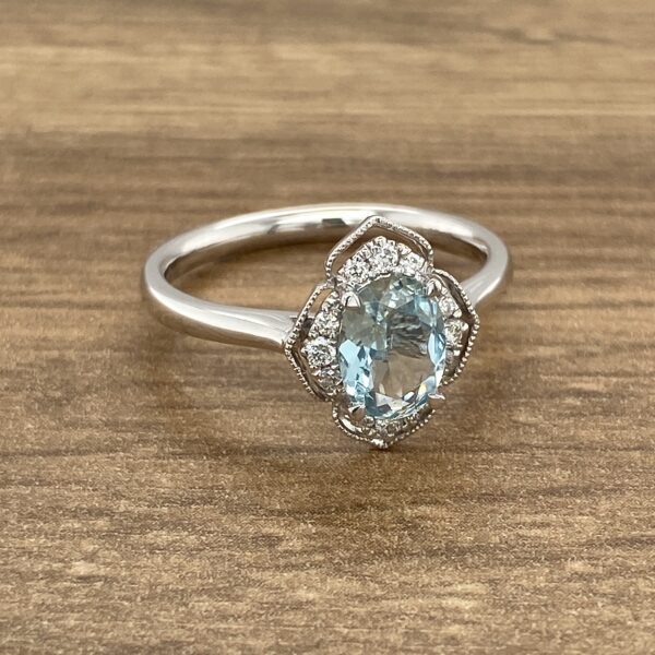 An oval aquamarine and diamond ring on a wooden table.