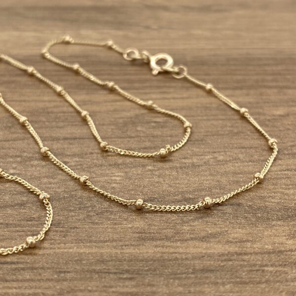 Three gold beaded chains on wood.