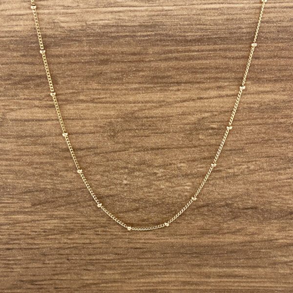 Gold beaded chain necklace on wood.