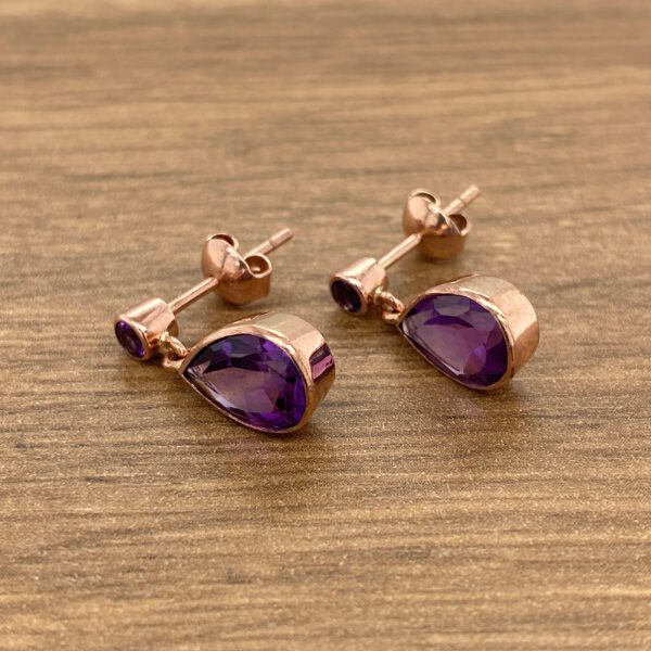 Rose gold earrings with purple teardrop stones.