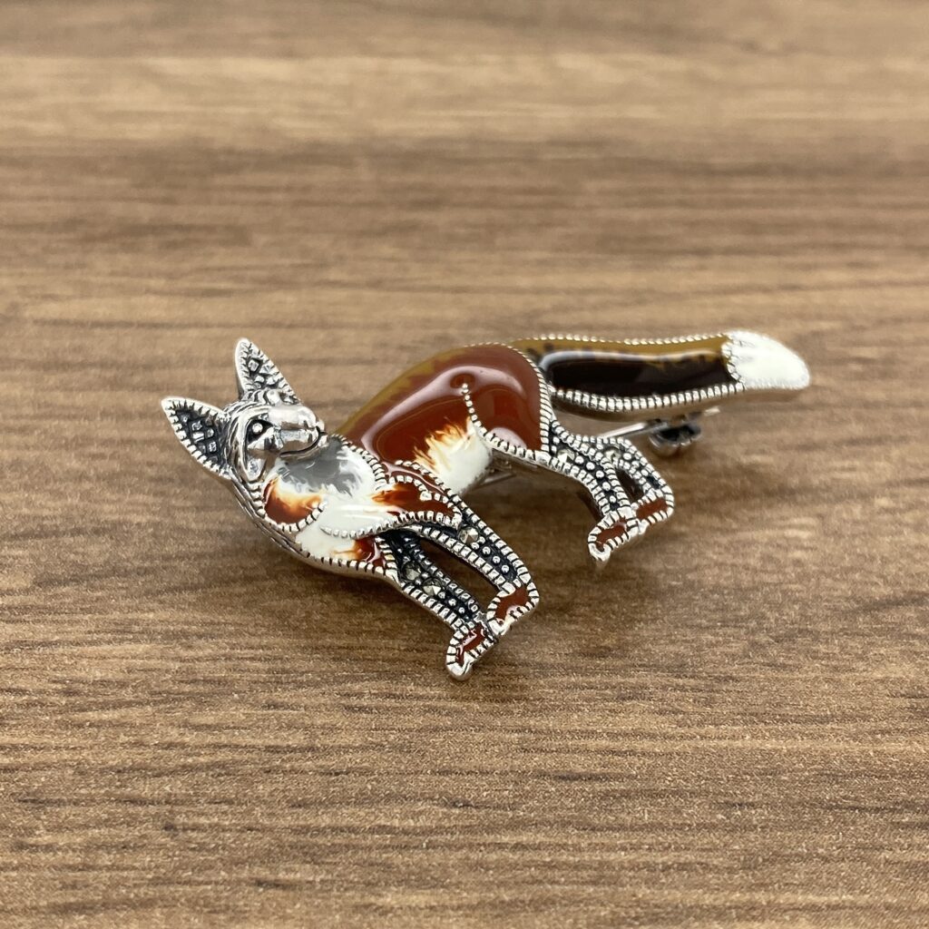 A Silver & Marcasite Enamel Fox Brooch on a wooden table.
