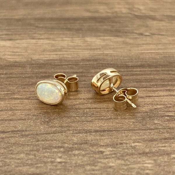 Gold opal earrings on wood background.
