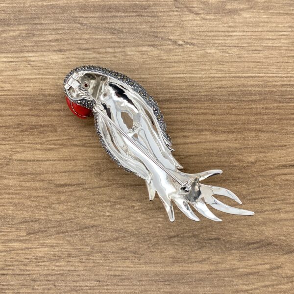 Silver and red bird brooch on wood.